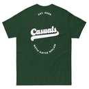 Forest green short-sleeve t-shirt laid flat, showing the back design: a large white oval outline with 'Casuals' in bold white text, 'EST. 2025' above, and 'WITH KATIE NOLAN' curved below.