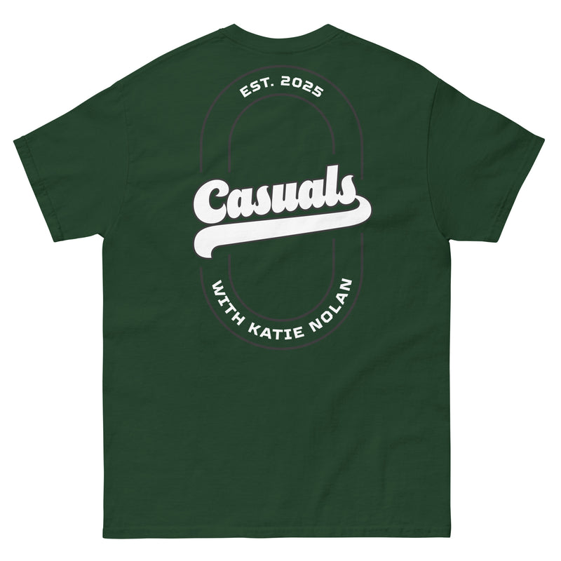 Forest green short-sleeve t-shirt laid flat, showing the back design: a large white oval outline with 'Casuals' in bold white text, 'EST. 2025' above, and 'WITH KATIE NOLAN' curved below.