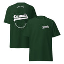 Forest green short-sleeve t-shirt shown from both angles. Front: small white logo on the left chest reading 'Casuals' with 'WITH KATIE NOLAN' below. Back: large oval outline with 'Casuals' in bold white text, 'EST. 2025' above, and 'WITH KATIE NOLAN' curved below.