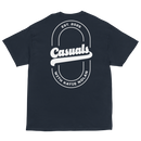 Navy short-sleeve t-shirt laid flat, featuring a large white oval outline on the back with bold text 'Casuals' in the center, 'EST. 2025' above, and curved text 'WITH KATIE NOLAN' below.