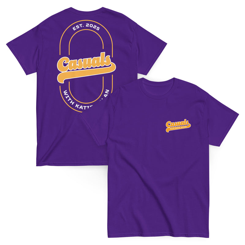 Two purple short-sleeve T-shirts laid flat, one showing the front and one showing the back. The front displays a small yellow and white 'Casuals WITH KATIE NOLAN' logo on the left chest, and the back features a large yellow 'Casuals' design with the text 'EST. 2025' and 'WITH KATIE NOLAN' arranged in a circular layout within a double-line oval.