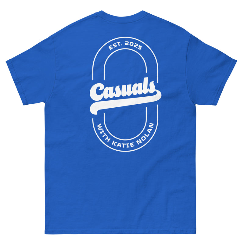 Royal blue short-sleeve t-shirt laid flat, showing the back design: a large white oval outline with 'Casuals' in bold across the center, 'EST. 2025' above, and 'WITH KATIE NOLAN' curved below.