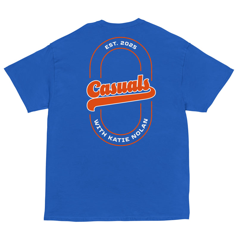 Bright royal blue short-sleeve T-shirt laid flat, showing a large back print with the word 'Casuals' in orange retro lettering across a double-line oval. Text around the oval reads 'EST. 2025' on top and 'WITH KATIE NOLAN' on the bottom.