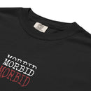 Close-up of the upper front of a black heavyweight T-shirt showing the ribbed crew neckline and part of the chest print. The word ‘MORBID’ is stacked three times in capital letters on the left chest area, with the top two lines in white and the bottom line in red. The fabric appears thick and smooth with subtle natural folds.