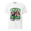 Front view of white unisex T-shirt featuring a large centered graphic reading ‘CONAN O’BRIEN’ in bold, glossy bright green three-dimensional block letters. Behind the text is a collage of Conan O’Brien in multiple looks and poses, including wearing a colorful futuristic helmet, clapping in a suit, playing an electric guitar, and flashing peace signs. Gray clouds and stylized lightning bolts create a dramatic, rock-concert style backdrop.