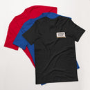 A top-down view of three stacked T-shirts in red, blue, and black heather. The black shirt on top displays a graphic with the text 'SAYONARA SUCKERS' and a rainbow underline.
