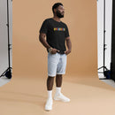 A man standing in a photo studio wearing a black heather T-shirt with the word 'BYEEEEEEEE' printed in colorful letters on the front. He is also wearing light denim shorts, white socks, and sneakers.