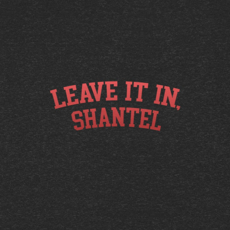 A close-up view of a black heather fabric showing red arched text printed on it. The text reads 'LEAVE IT IN, SHANTEL' in bold, all-caps lettering.