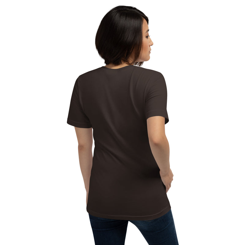 Solid brown short-sleeve t-shirt shown from the back with no visible graphics, worn by a woman standing with one hand on her hip.