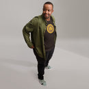 Solid brown short-sleeve t-shirt with the circular yellow and brown 'HEY NONG MAN' logo centered on the chest, worn by a man indoors with a green jacket layered over it.