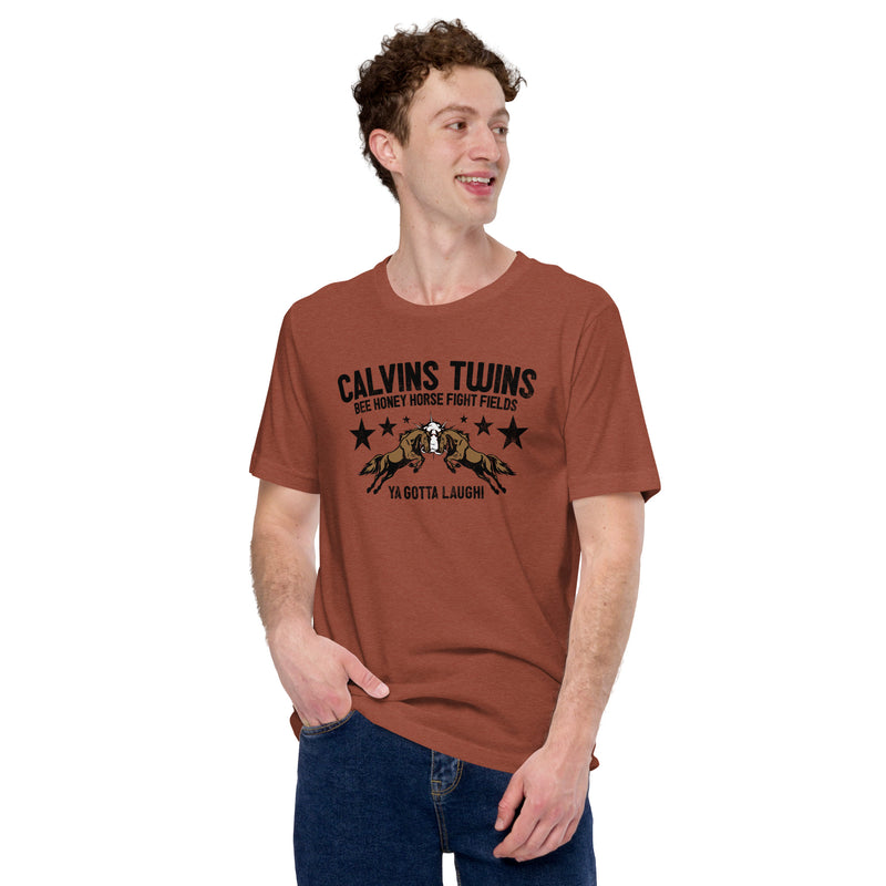 Heather clay short-sleeve t-shirt with black text 'CALVINS TWINS' and horse collision graphic with stars, plus smaller text 'BEE HONEY HORSE FIGHT FIELDS' and 'YA GOTTA LAUGH!' Worn by a man standing with one hand in his pocket, smiling off to the side.