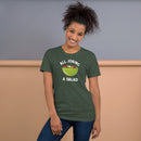 Heather forest short-sleeve t-shirt with a green salad bowl graphic and white text 'ALL JOKING A SALAD', worn by a smiling woman standing indoors against a two-tone beige and gray wall.