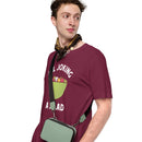 Maroon short-sleeve t-shirt with a green salad bowl graphic and white text 'ALL JOKING A SALAD', worn by a man carrying a crossbody bag and accessorized with a scarf, looking off to the side.