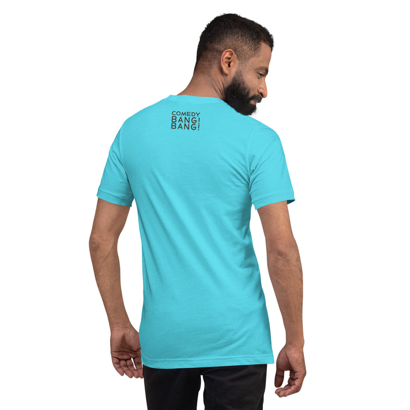 A man facing away from the camera wearing a turquoise t-shirt with a small black 'COMEDY BANG! BANG!' logo printed at the upper back near the neckline.