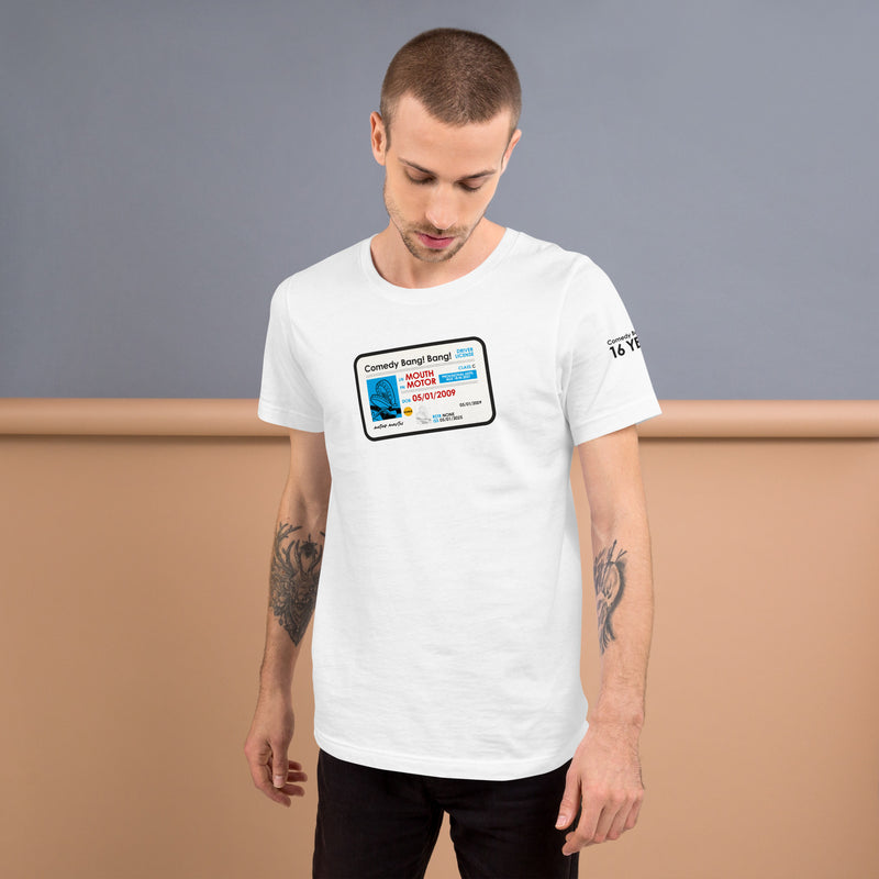 A man with arm tattoos wearing a white t-shirt with the 'Comedy Bang! Bang!' license graphic centered on the chest and 'Comedy Bang! Bang! 16 YEARS' printed in black is partially visible on the left sleeve.