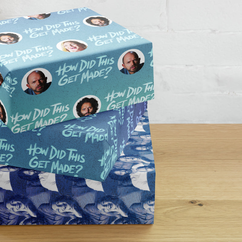 Stack of decorative boxes with 'How Did This Get Made' logo and images on a wooden surface against a white brick wall.
