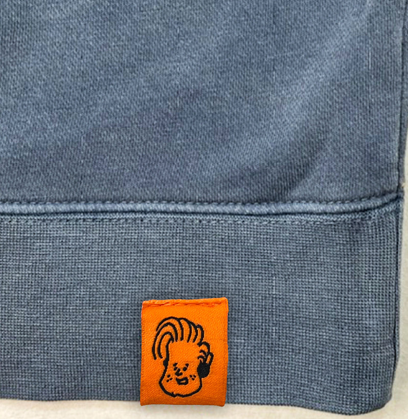 Label on clothing featuring a cartoon illustration of Conan with headphones and distinctive hair on an orange background.