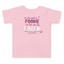 A pink t-shirt with text: 'I'm not a FOODIE I'm an EATER' surrounded by food illustrations and the small 'The Sporkful' logo below.