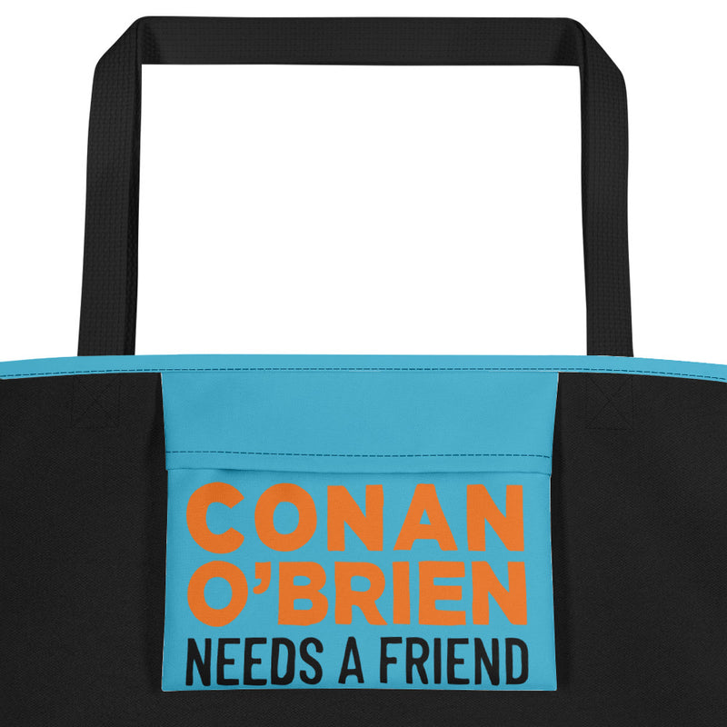 Close up of inside pocket of a teal beach bag with black handles, featuring colorful text reading 'CONAN O'BRIEN NEEDS A FRIEND.' 