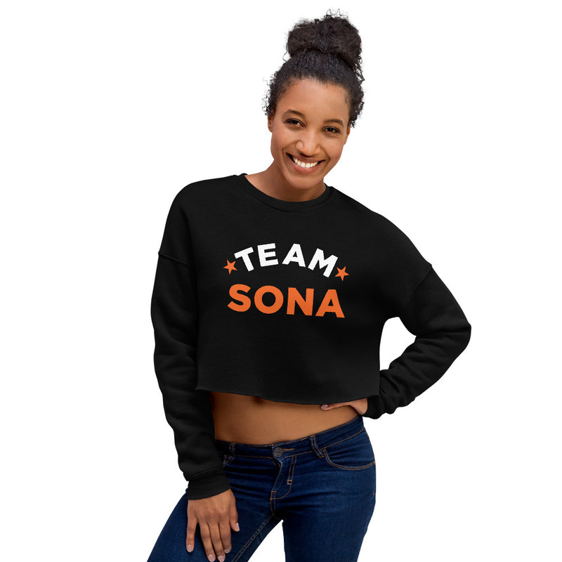 Woman smiling in black cropped sweatshirt with 'TEAM SONA' printed on front in white and orange lettering.