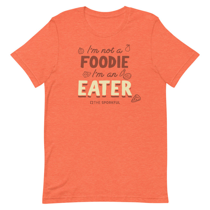 Orange t-shirt with text: 'I'm not a FOODIE I'm an EATER' surrounded by food illustrations and the small 'The Sporkful' logo below.