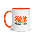 White mug with orange interior and handle featuring the text 'Conan O'Brien Needs A Friend' in bold black and orange letters.