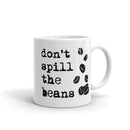 Backside of white mug features the text 'Don't spill the beans' and coffee beans graphic design.